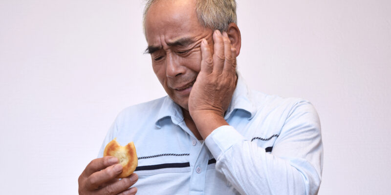 elderly man holding his jaw in tooth pain after biting a bagel