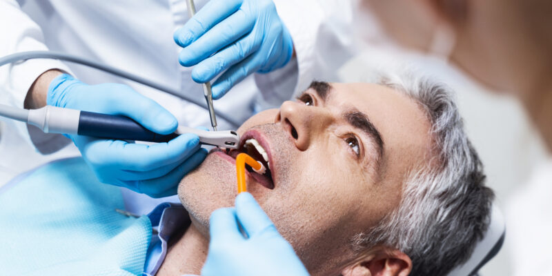 Male is lying in dental chair and being given root canal by dentist and assistant