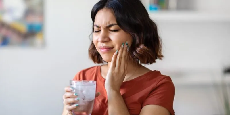 Sensitive Teeth. Young woman drinking water with ice and touching her cheek, dental pain