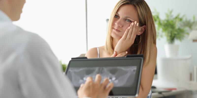 young woman with severe tooth pain being showed and x-ray by a dentist