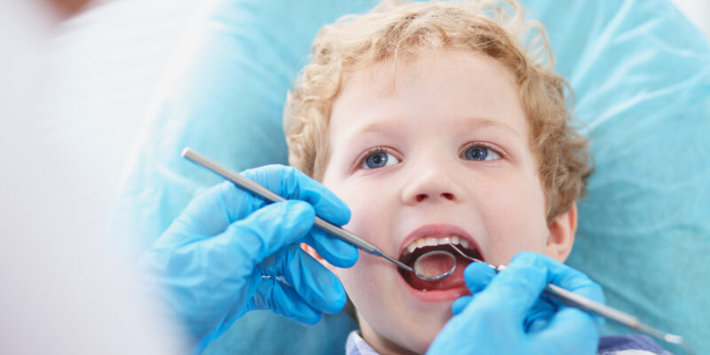 little boy having his teeth examined by a dentist in blue gloves