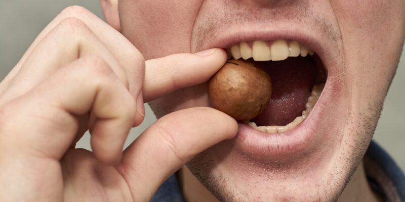 A man tries to crack a macadamia nut between his teeth