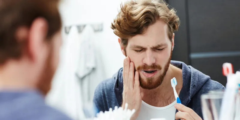 man with sensitive tooth brushing his teeth in mirror